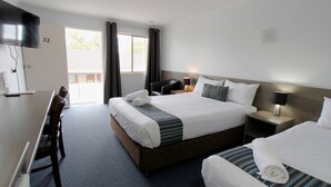 Ein Hotelzimmer mit einem großen Bett, einem kleineren Bett, einem Schreibtisch mit Stuhl, einem Fernseher und einem Fenster mit Vorhängen.