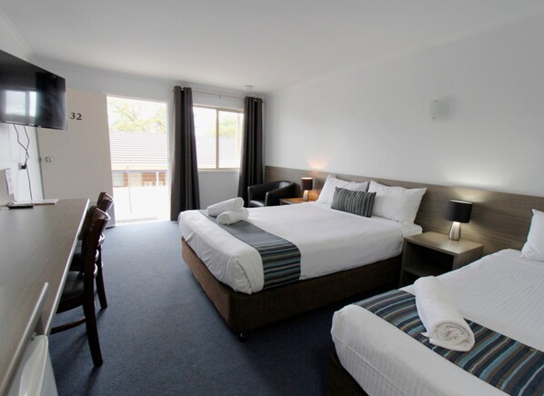 A hotel room with a large bed, a smaller bed, a desk with a chair, a TV, and a window with curtains.