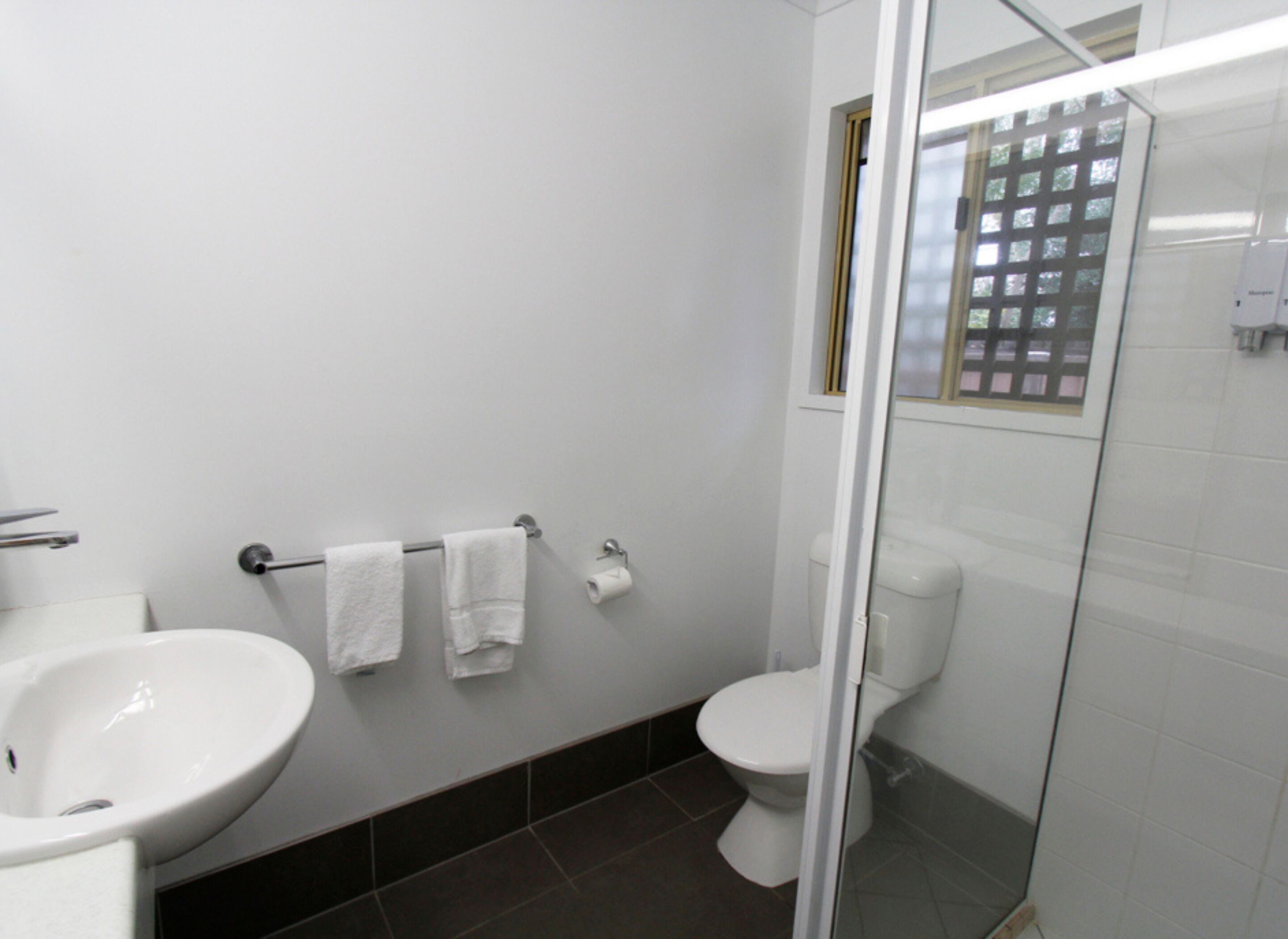 Un baño con un lavamanos blanco, dos toallas blancas, un inodoro y una cabina de ducha de cristal.