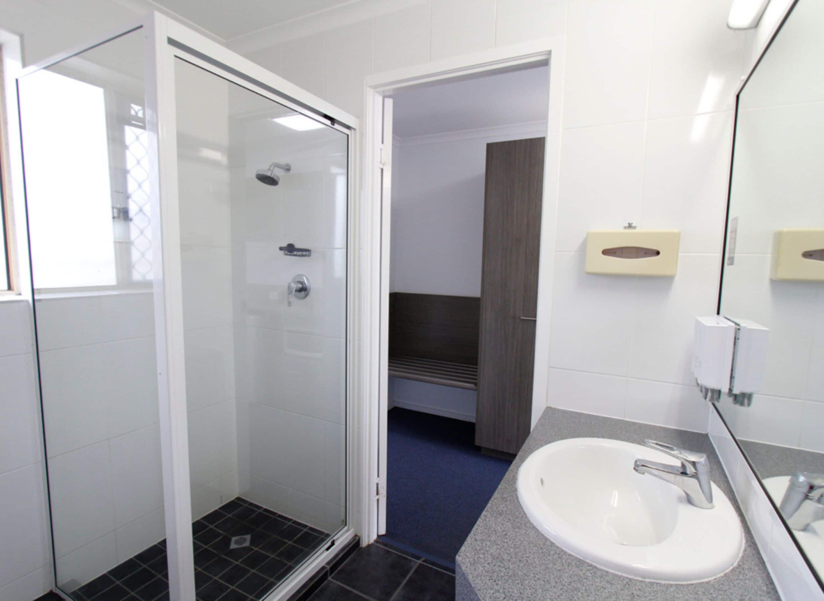 A modern bathroom with a glass shower enclosure, a white sink with a granite countertop, and a mirror with a towel dispenser.