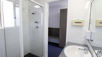 A modern bathroom with a glass shower enclosure, a white sink with a granite countertop, and a mirror with a towel dispenser.