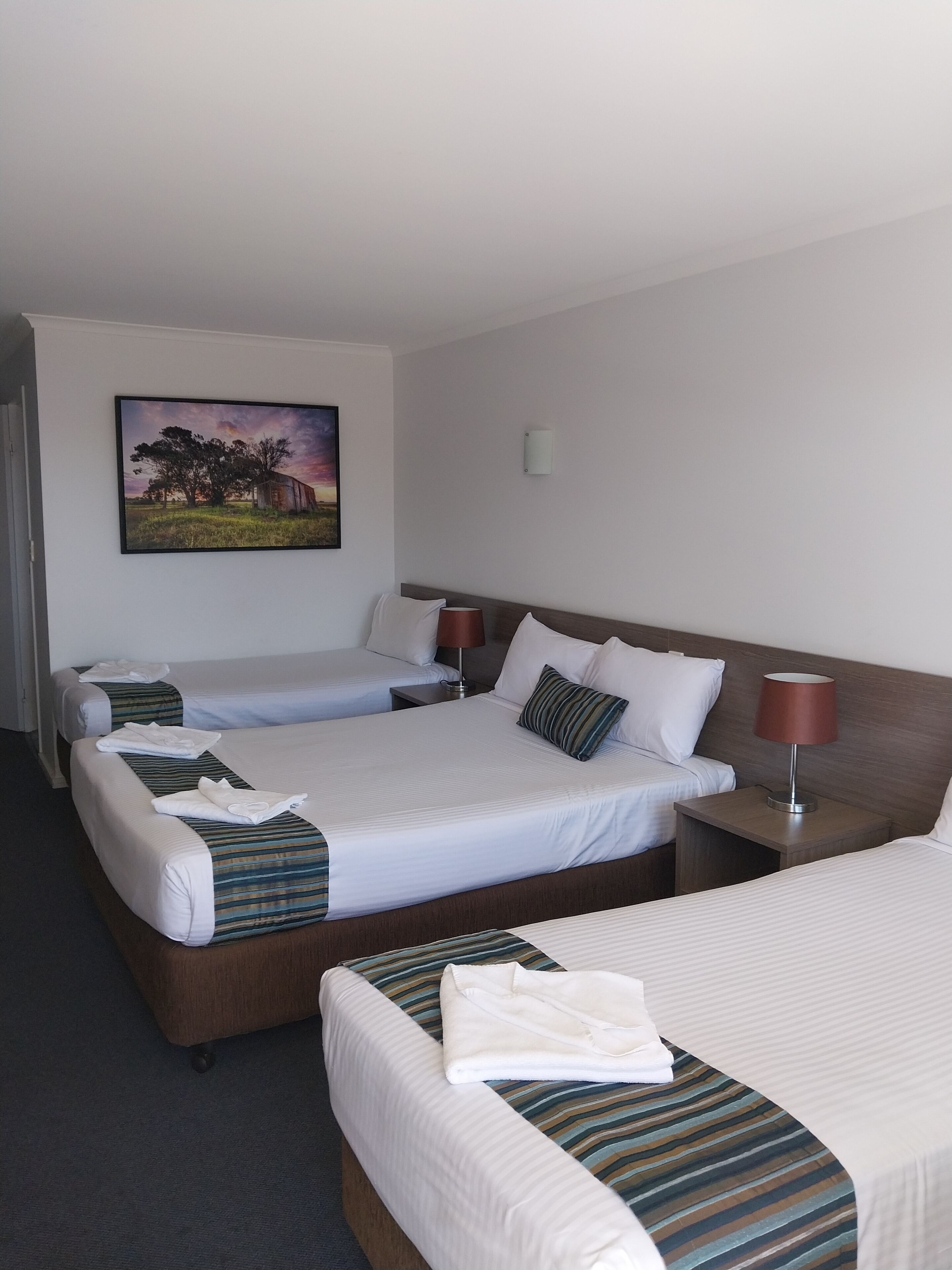 Habitación de hotel con tres camas, un cuadro en la pared y una lámpara en la mesita de noche.