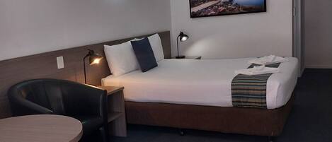A hotel room with a bed, a desk, a chair, a small table, and a wall-mounted picture.