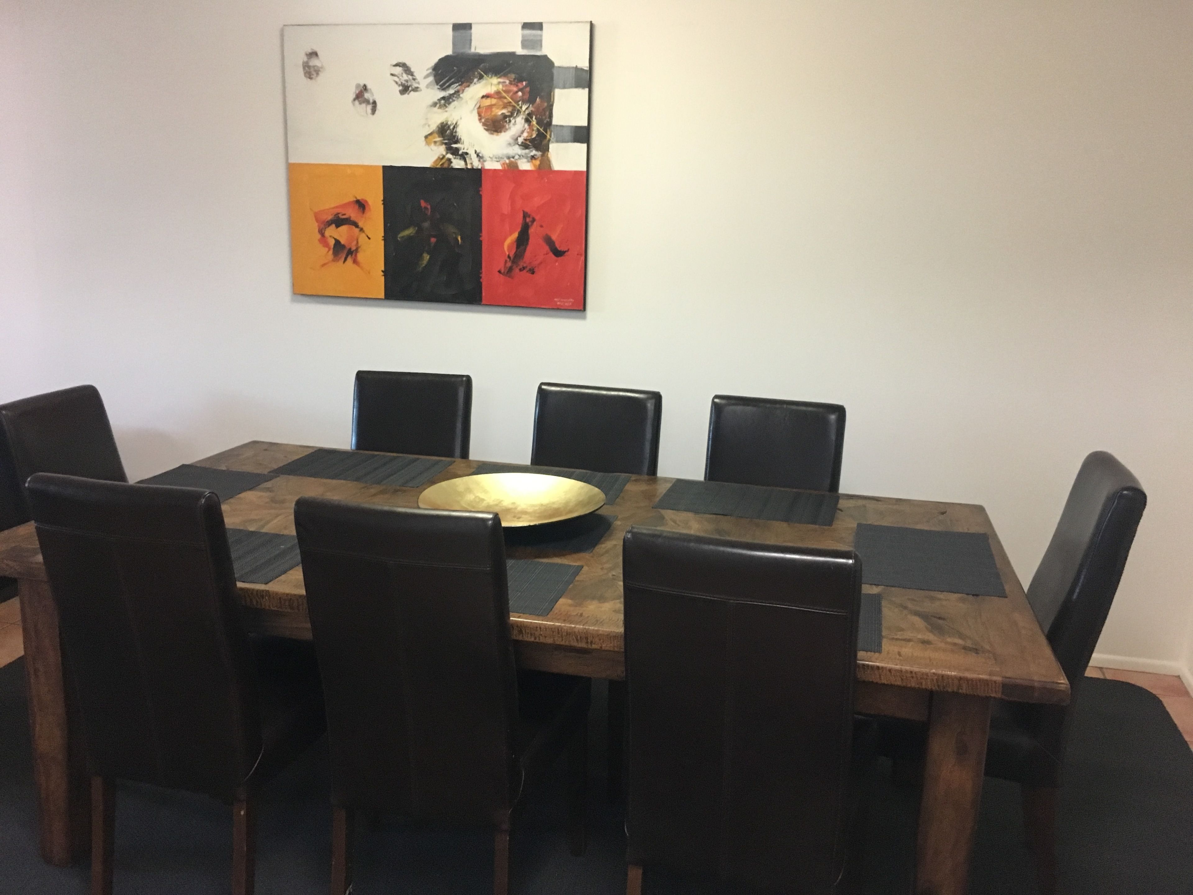 A conference room with a wooden table, black chairs, and a colorful abstract painting on the wall.
