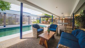 A covered outdoor area with a pool, wicker furniture, and a table. - The Cosmopolitan Motel and Serviced Apartments (Rockhampton)