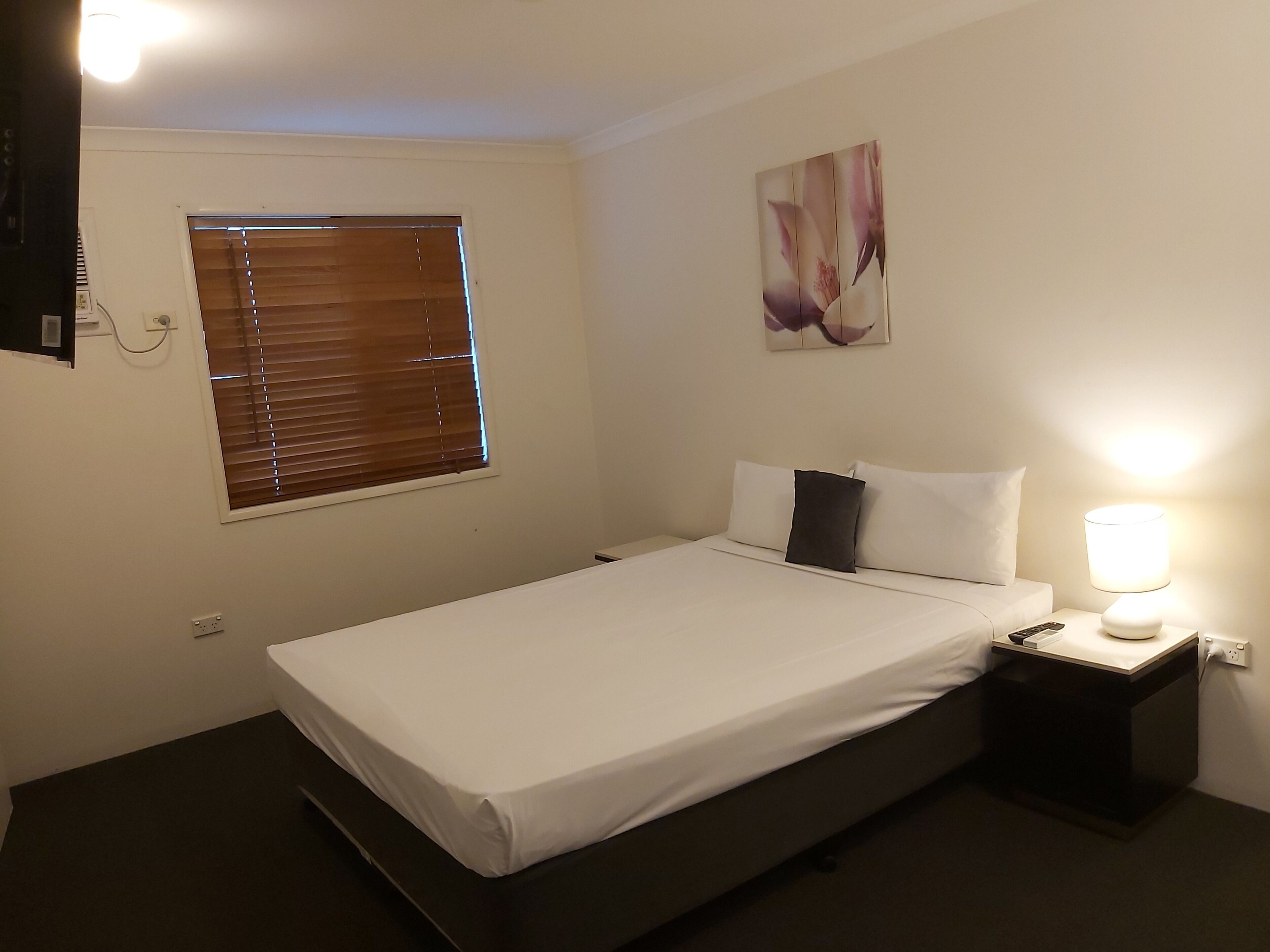 A neatly made bed with white linens, a bedside lamp, and a wall-mounted painting.