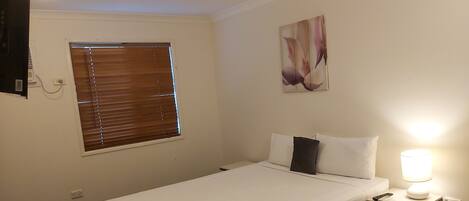 A neatly made bed with white linens, a bedside lamp, and a wall-mounted painting.