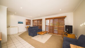 A living room with a sofa, a coffee table, a television, and a kitchen area with cabinets and a countertop. - The Cosmopolitan Motel and Serviced Apartments (Rockhampton)