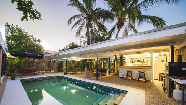 A swimming pool with a tiled deck, a bar area with stools, and a seating area with a table and chairs. - The Cosmopolitan Motel and Serviced Apartments (Rockhampton)