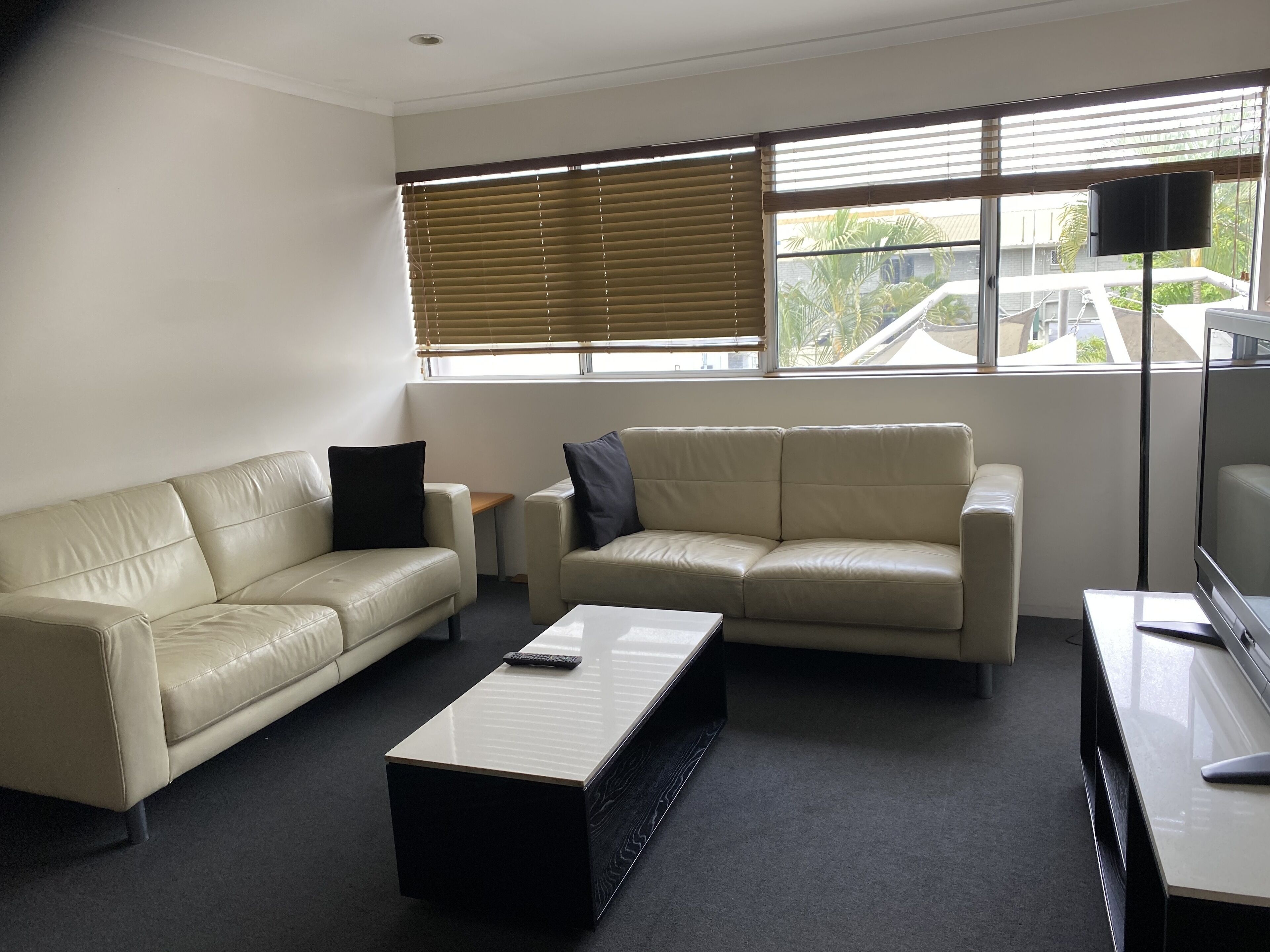 A modern living room with two beige leather sofas, a coffee table, and a flat-screen TV.