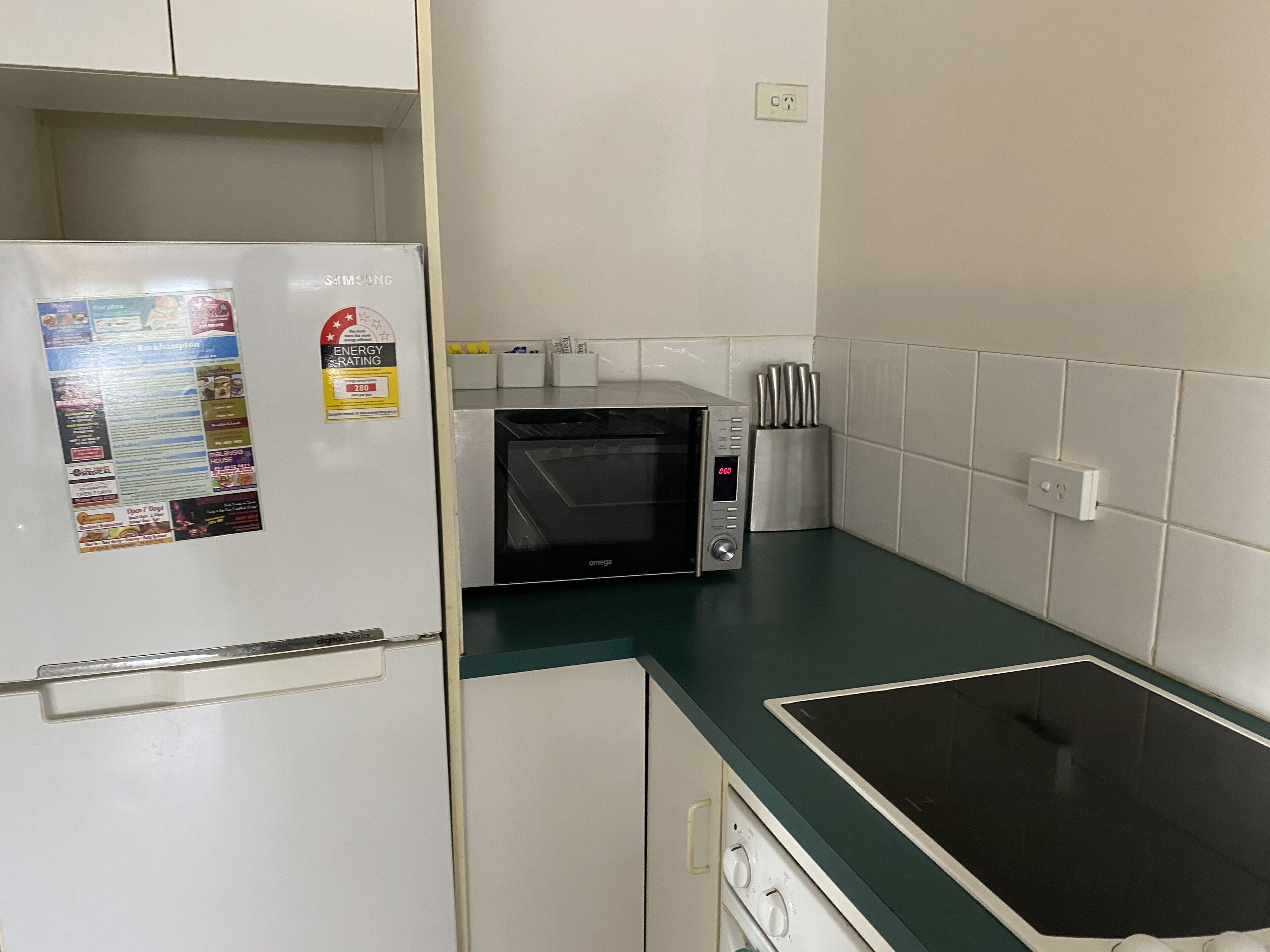 Una cocina con un refrigerador blanco, un microondas y una cocina por inducción negra.