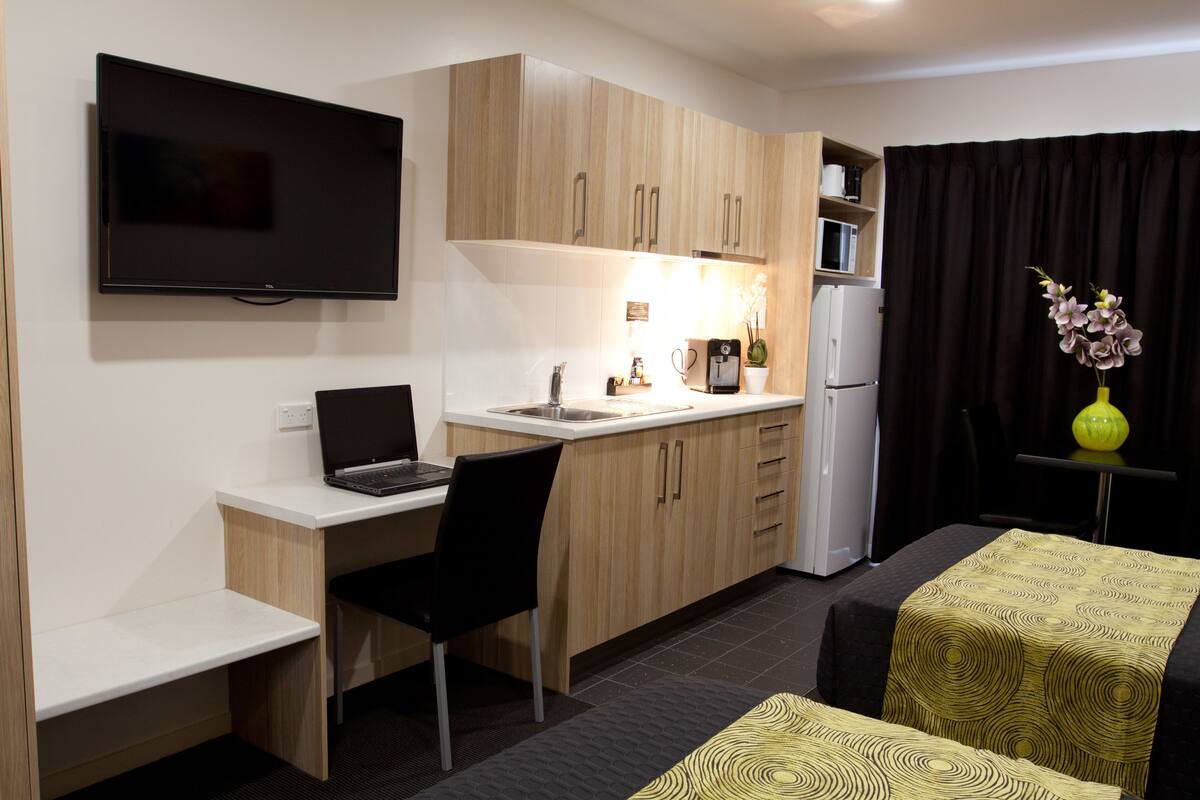 A compact kitchen with a flat-screen TV, a laptop, a coffee machine, and a refrigerator.