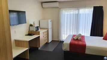 A hotel room with a bed, a desk, a microwave, a refrigerator, a TV, and a ceiling fan.
