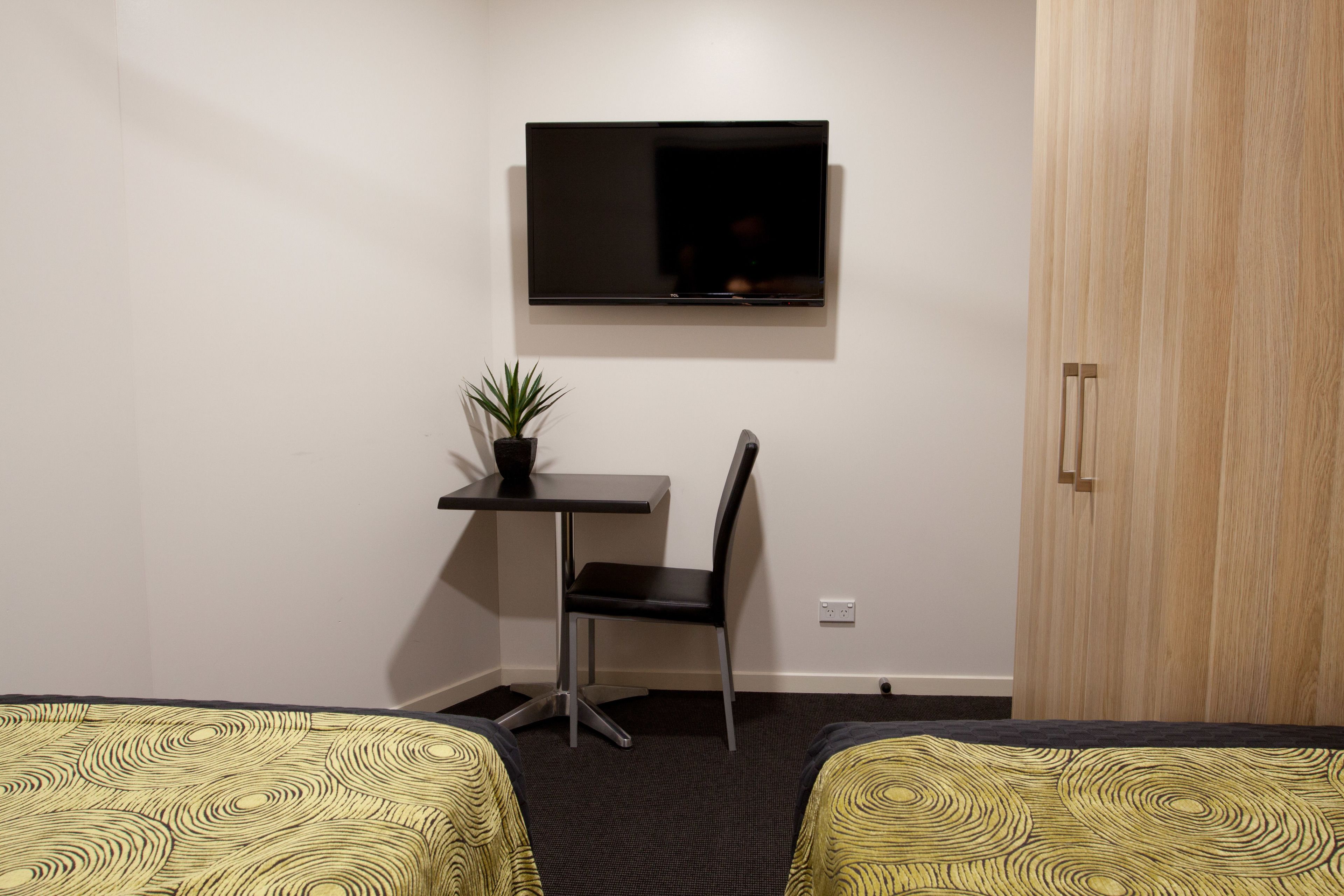 A hotel room with two beds, a desk with a chair, a TV mounted on the wall, and a wardrobe.
