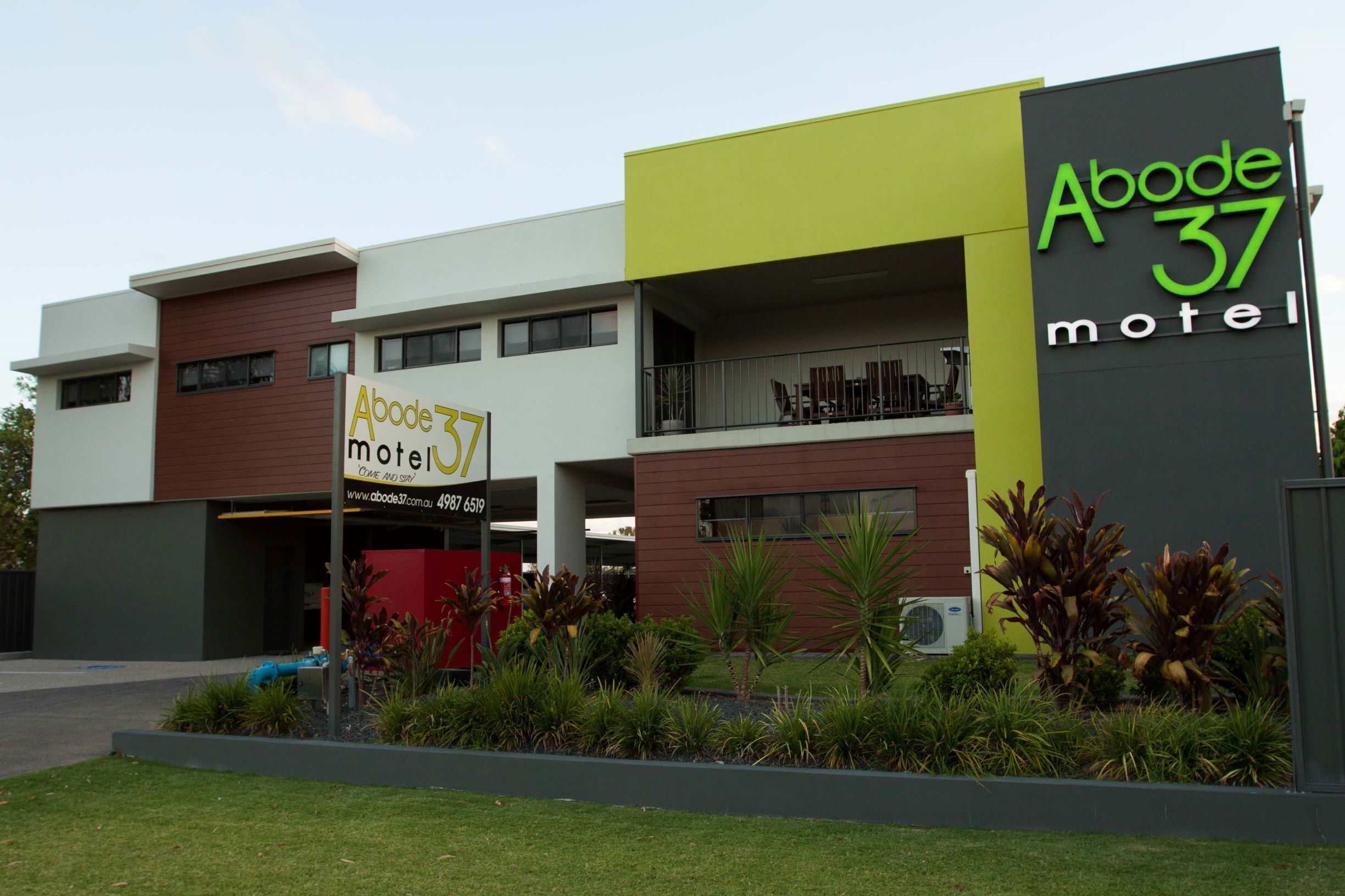 A modern motel with a prominent sign, a balcony, and a landscaped garden area.