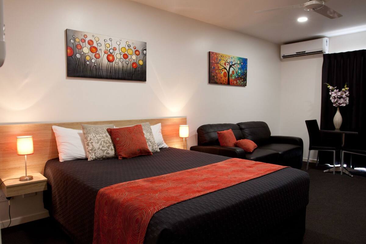 A hotel room with a bed, a sofa, a desk, and two paintings on the wall.
