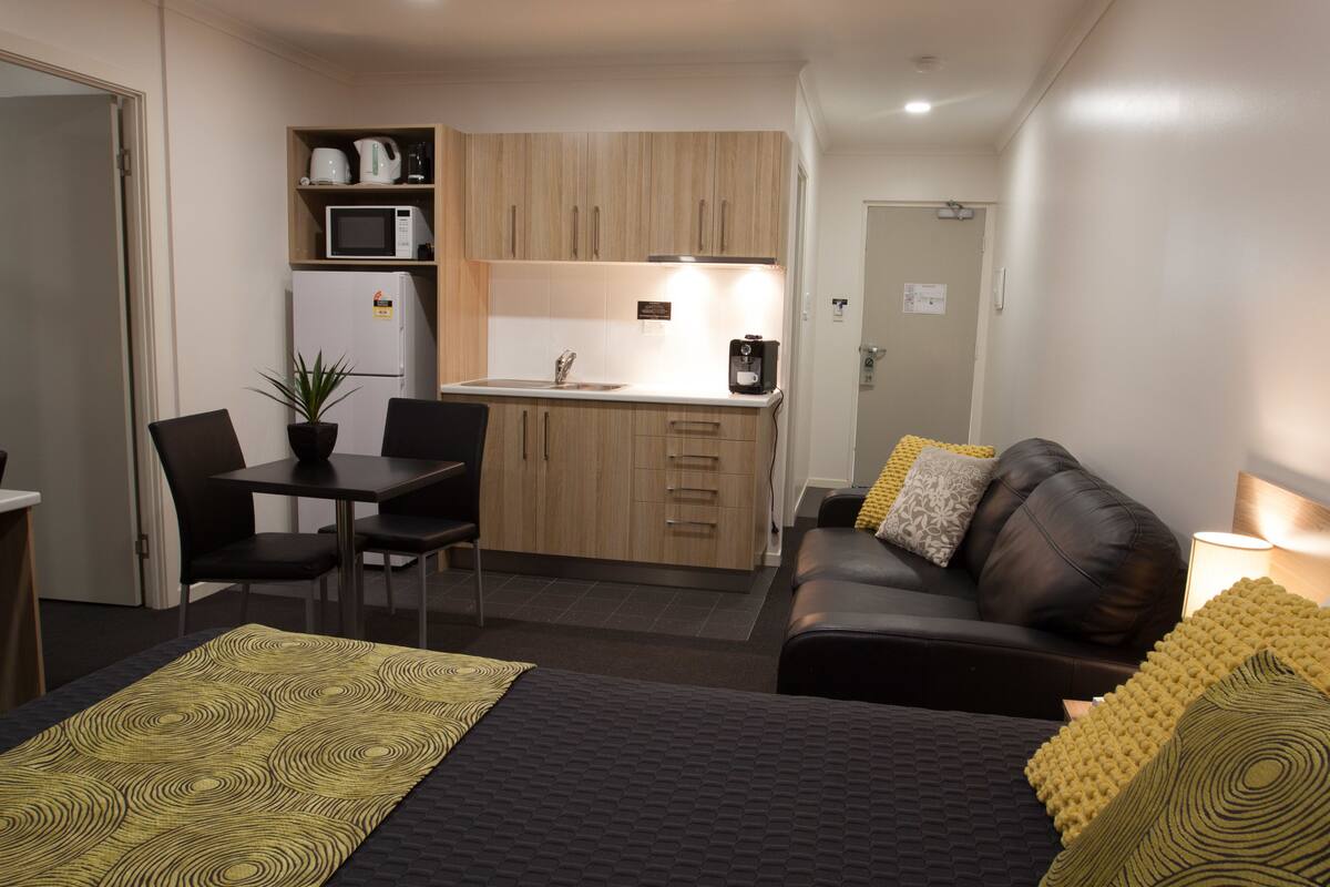 A compact hotel room with a kitchenette, a dining area, a sofa, and a bed.