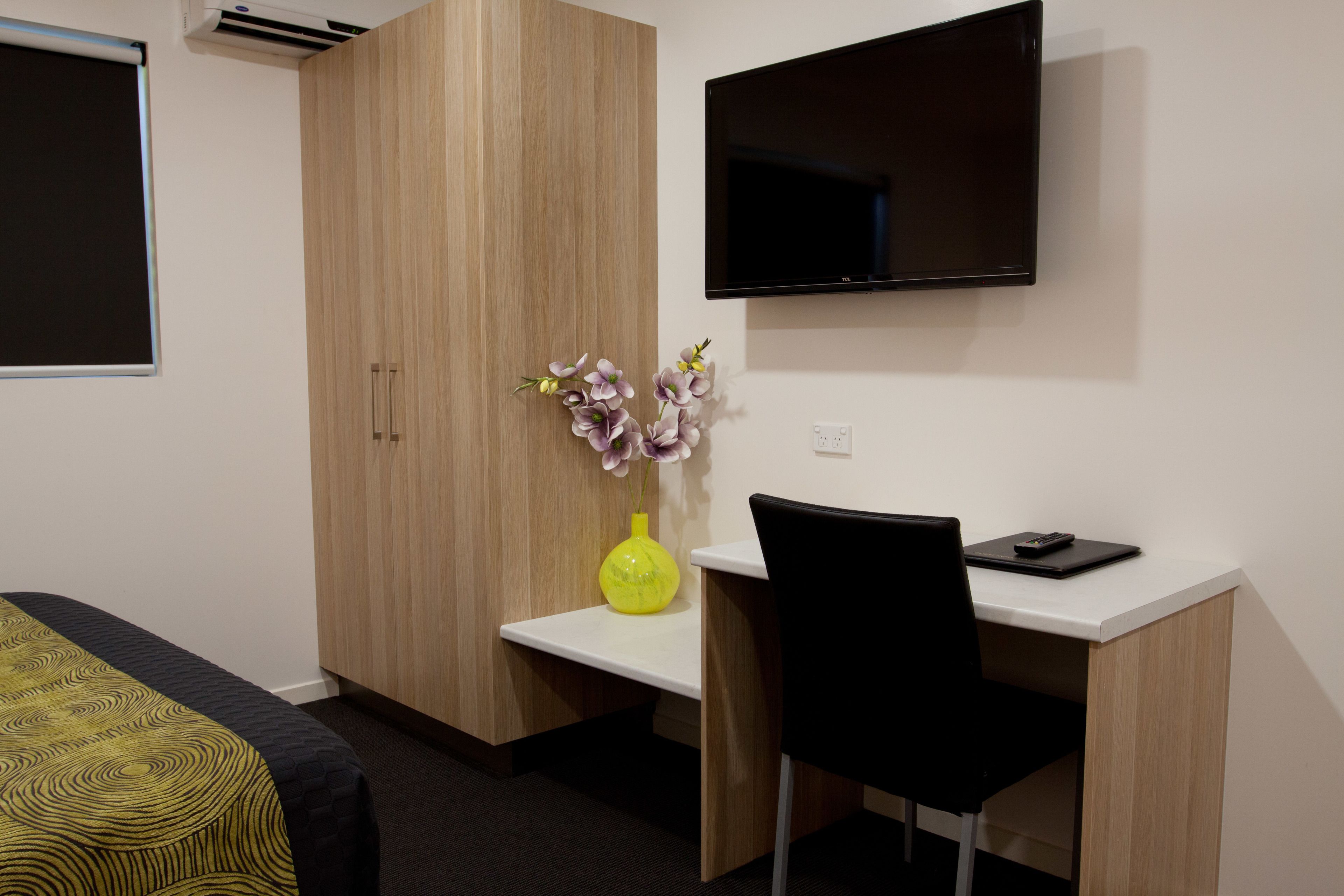 A hotel room with a bed, a desk, a chair, a TV, and a vase with flowers.