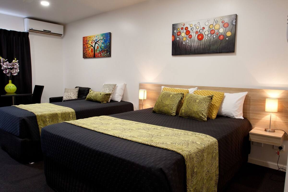 A hotel room with two beds, a desk, a chair, and artwork on the walls.