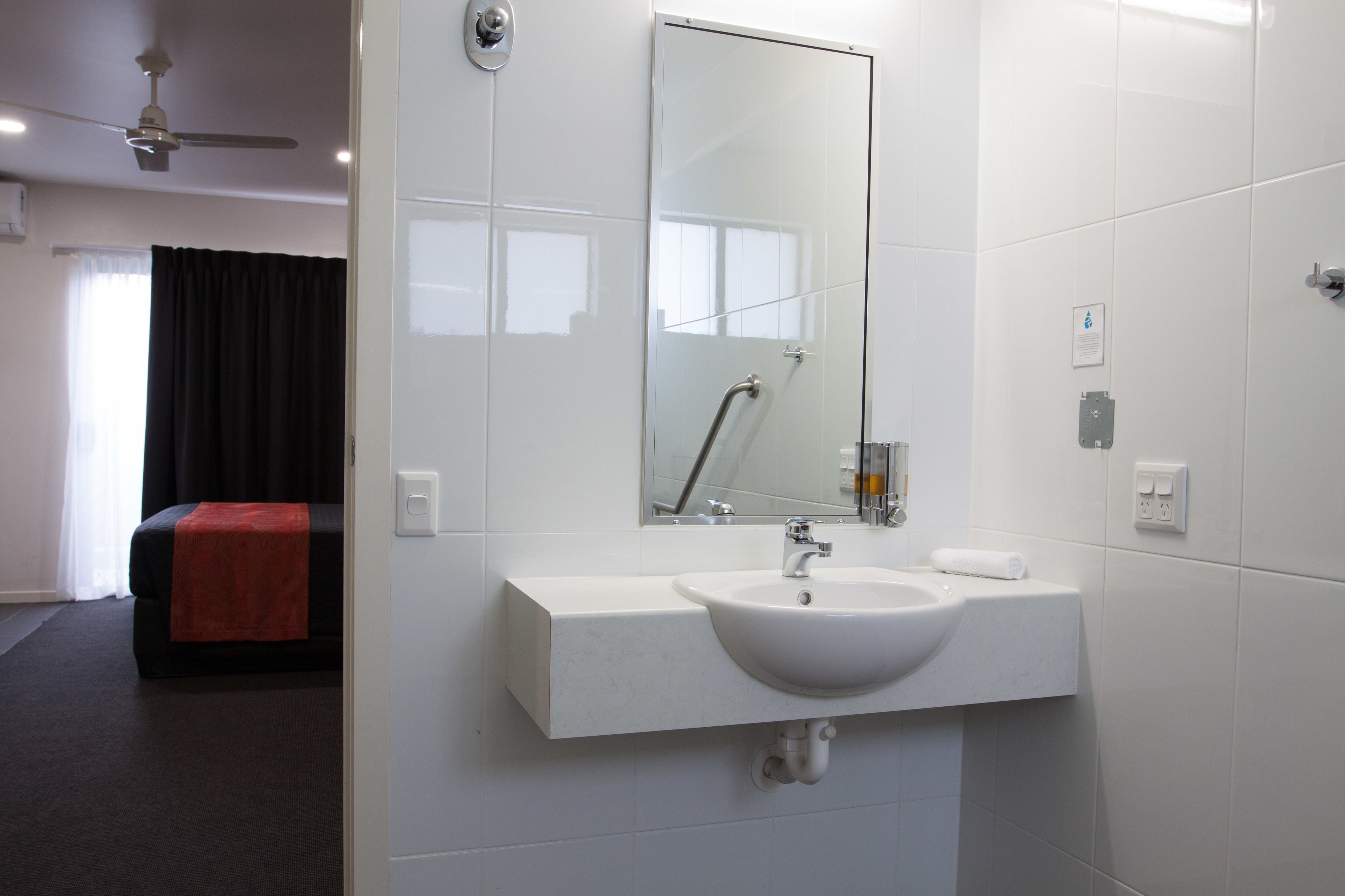 Een hotelbadkamer met een wit wastafel, spiegel en betegelde muren.