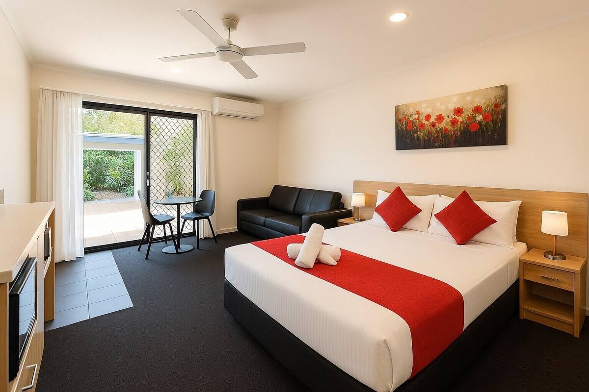 A hotel room with a bed, a desk, a chair, a couch, a painting, and a ceiling fan.