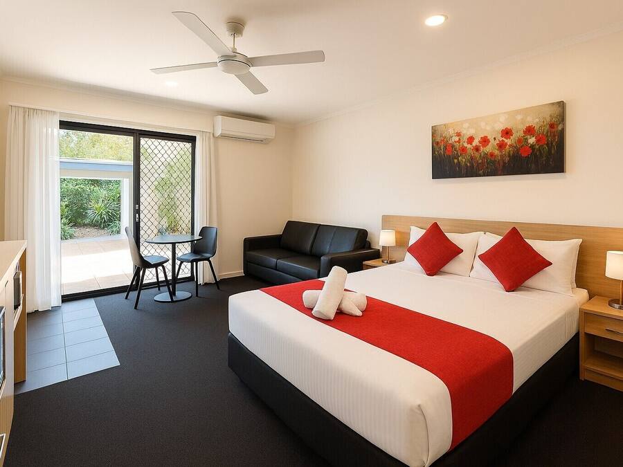Una habitación de hotel con cama, escritorio, silla, sofá, un cuadro y ventilador de techo.