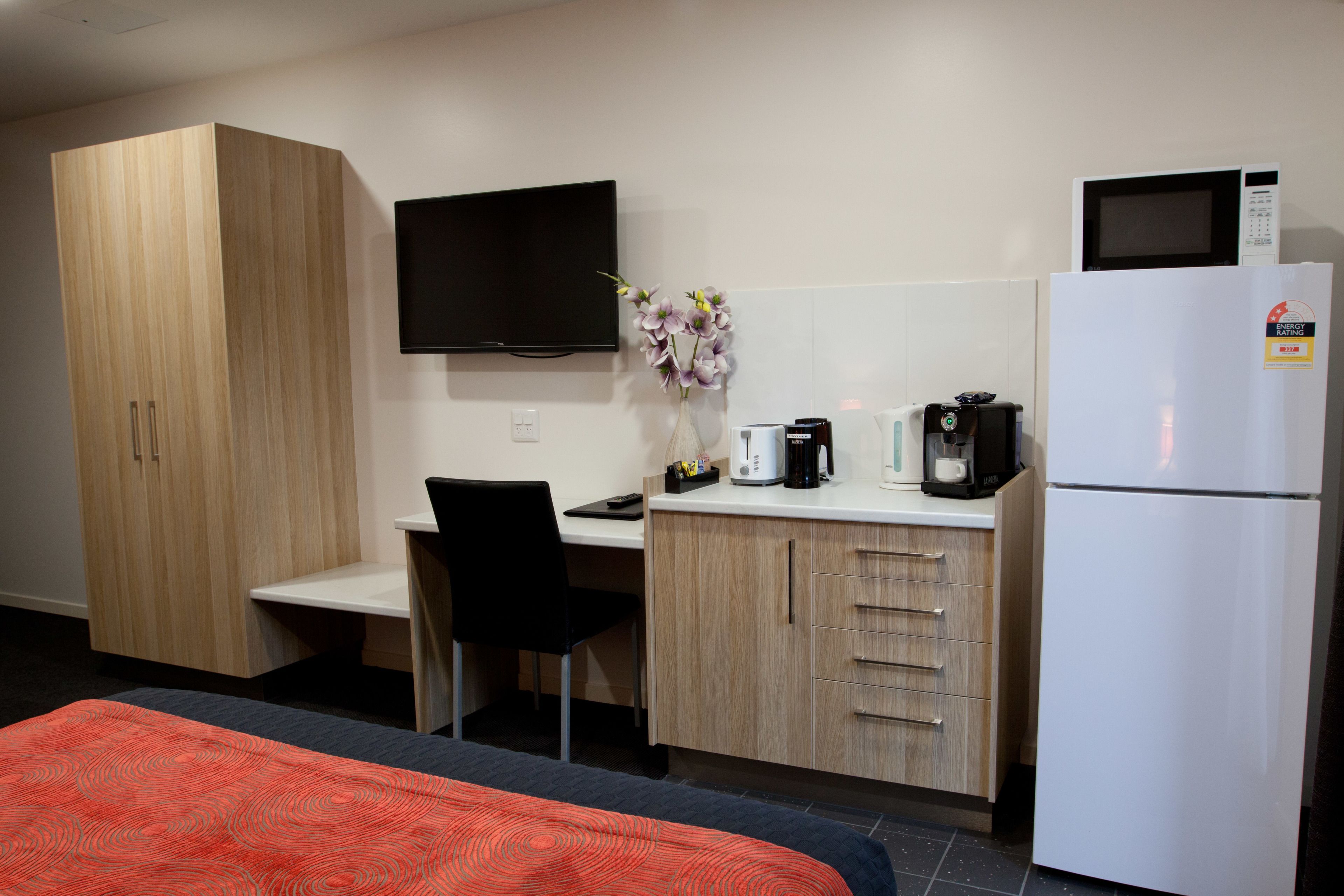 A hotel room with a bed, a desk, a chair, a television, a refrigerator, and a microwave.