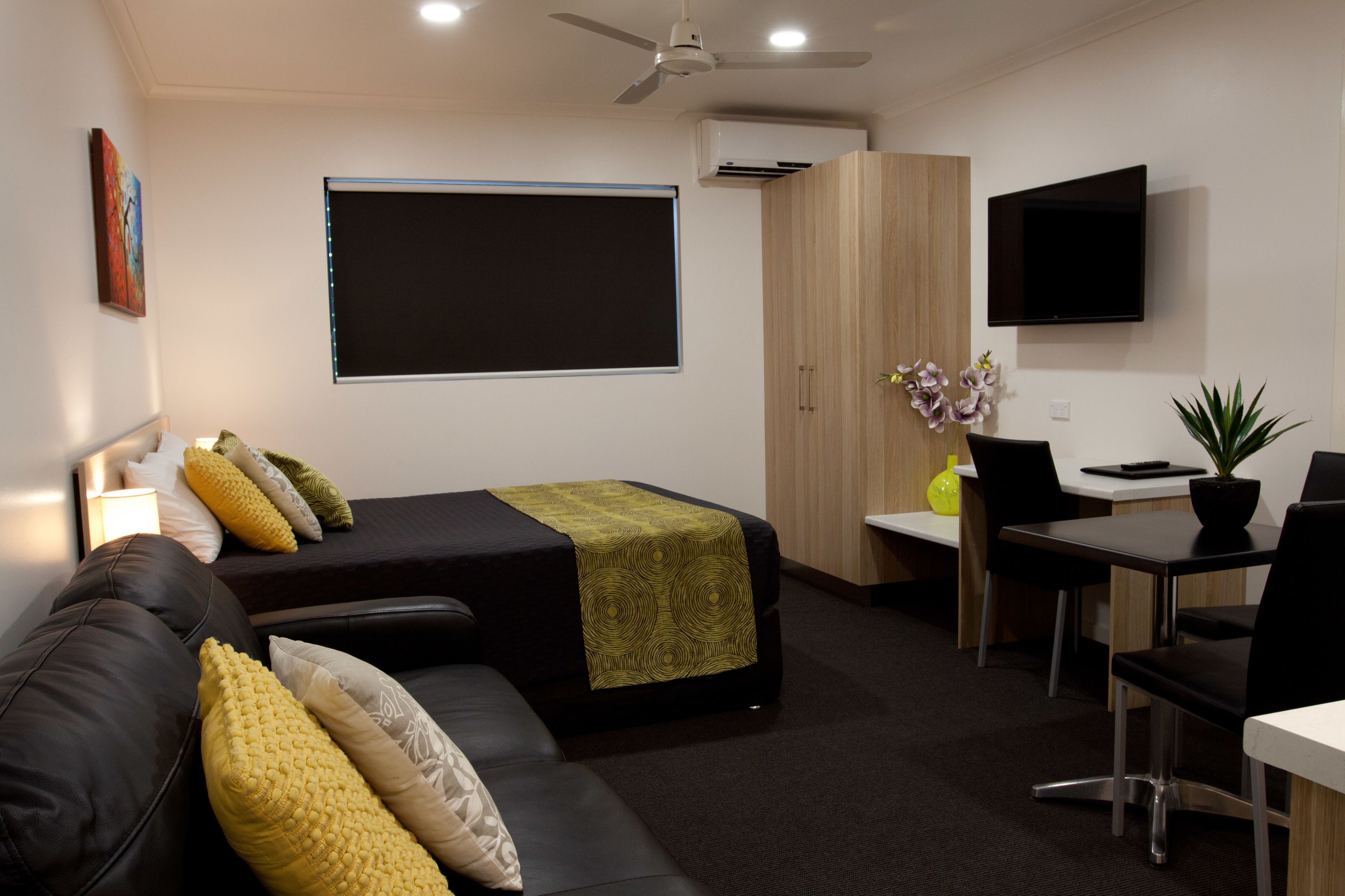 A modern hotel room with a bed, a desk, a chair, a TV, and a ceiling fan.