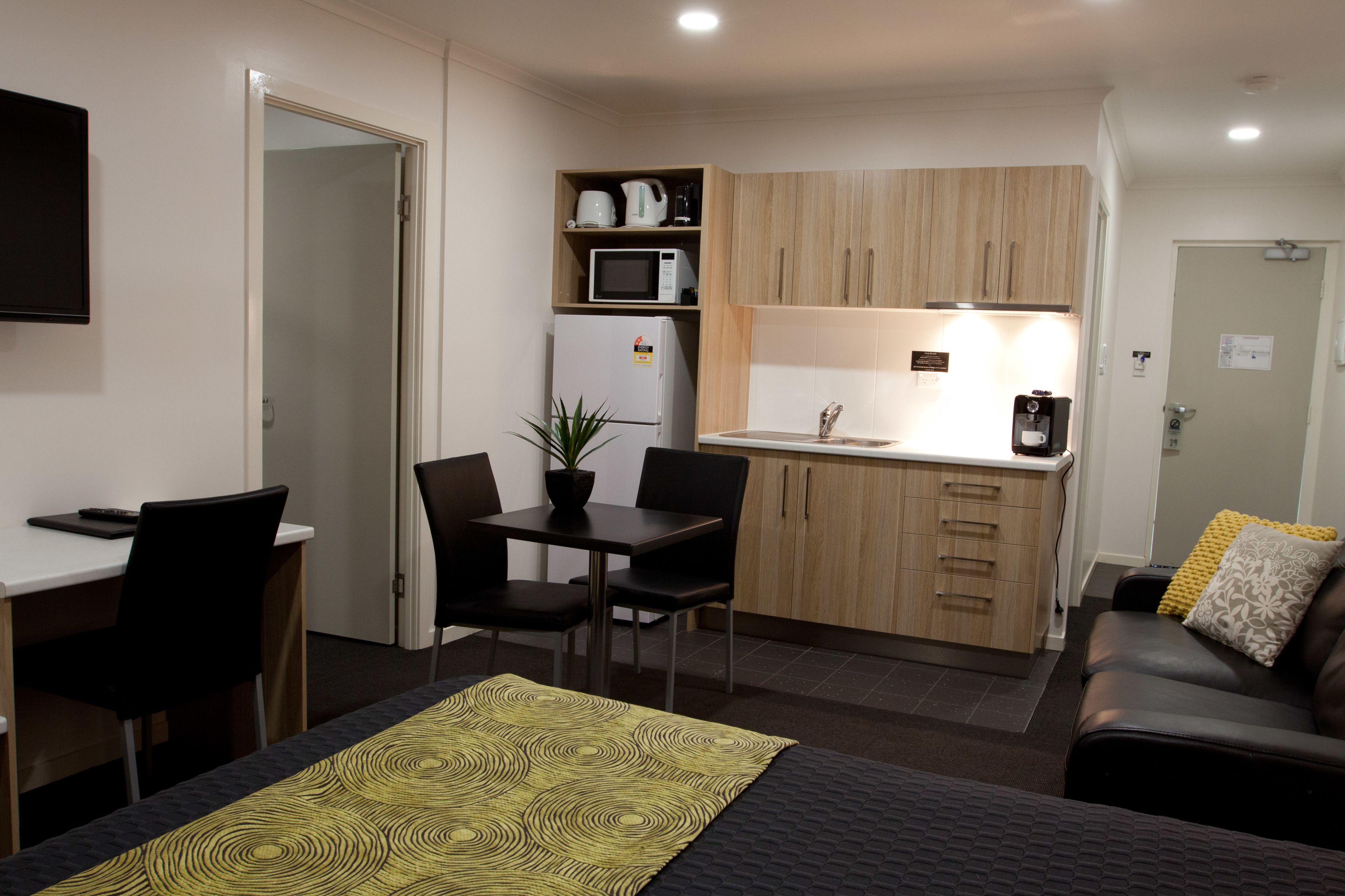A compact hotel room with a kitchenette, a dining area, and a seating area with a couch.