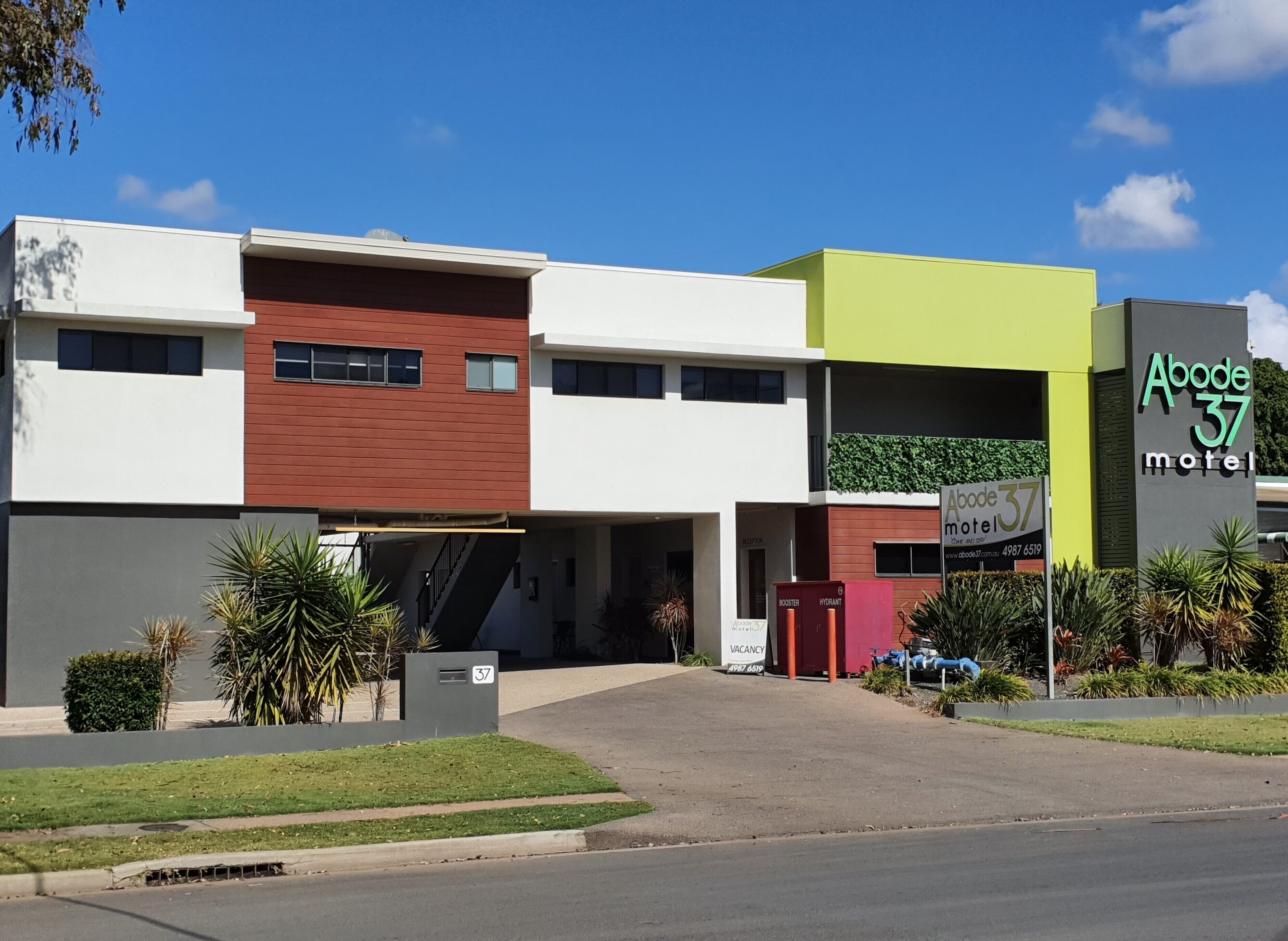 A modern building with a sign for Abode 37 Motel, featuring a flat roof, a red and white facade, and a green accent wall.