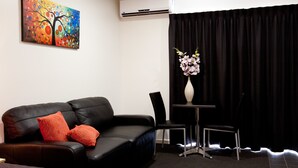 Una habitación de hotel moderna con un sofá de cuero negro, una mesita con un florero y un cuadro en la pared.
