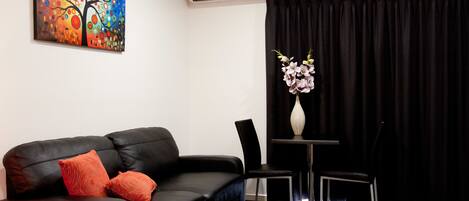 A modern hotel room with a black leather sofa, a small table with a vase of flowers, and a painting on the wall.