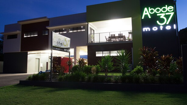 Un motel moderno con un letrero de neón llamativo, un balcón con mobiliario exterior y un césped bien cuidado.