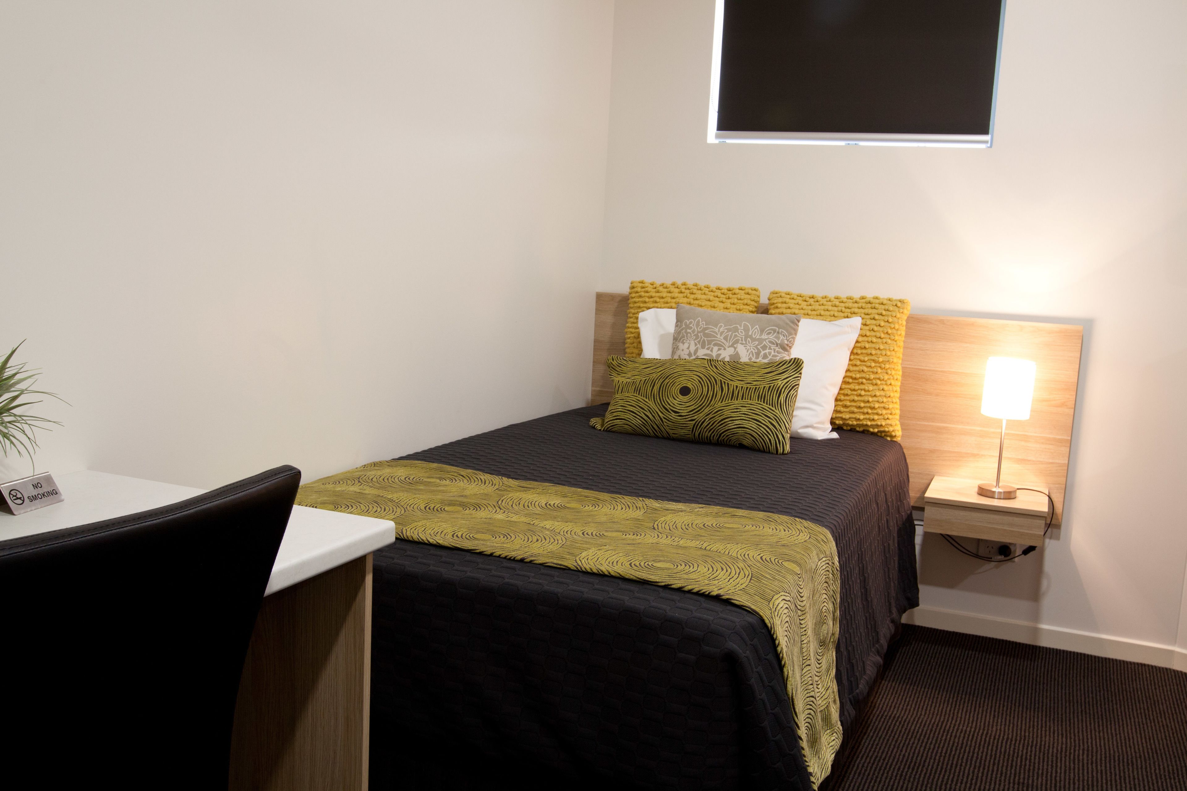 Un dormitorio ordenado con cama, mesita de noche y un escritorio pequeño.