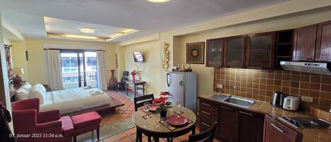 A hotel room with a bed, a dining table with chairs, a kitchen area with cabinets and a sink, and a TV on the wall.