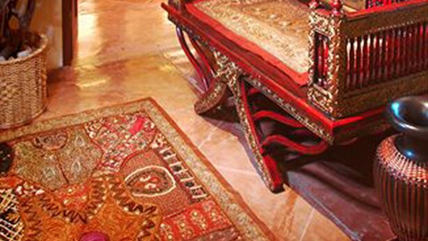 Une pièce au décor traditionnel, avec un canapé en bois, une grande plante en pot et un tapis à motifs.