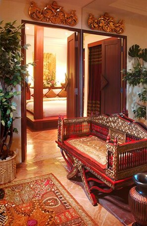A traditional room with a wooden sofa, a large potted plant, and a patterned rug. - Nirvana Boutique Suites (Pattaya)