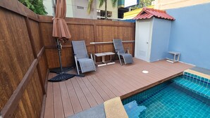 Une terrasse en bois avec une piscine, deux chaises longues, une petite table et une porte.