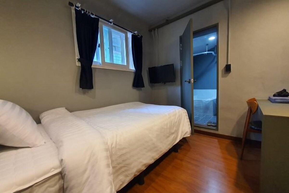 A bedroom with a bed, a TV mounted on the wall, a window with curtains, and a door leading to a balcony.