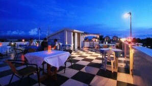 Un área de comedor al aire libre con piso a cuadros, mesas y sillas, bajo un cielo despejado.