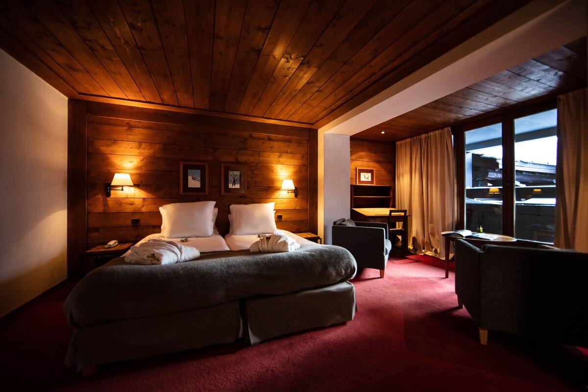 A hotel room with a wooden ceiling, a large bed with pillows, a desk, and a chair.