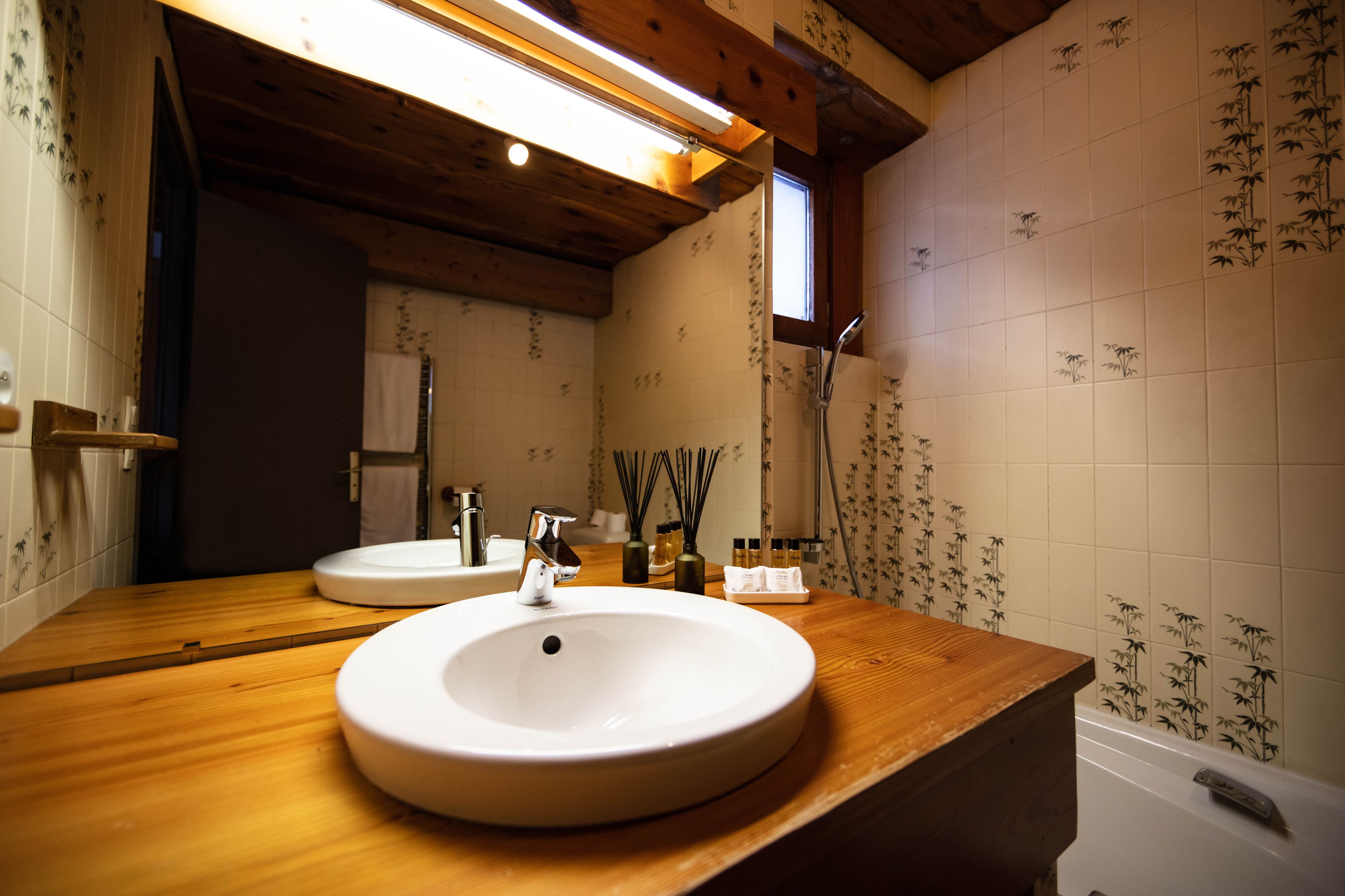 Une salle de bain avec un meuble-lavabo en bois, un lavabo rond, un miroir et des carreaux à motifs de bambou.