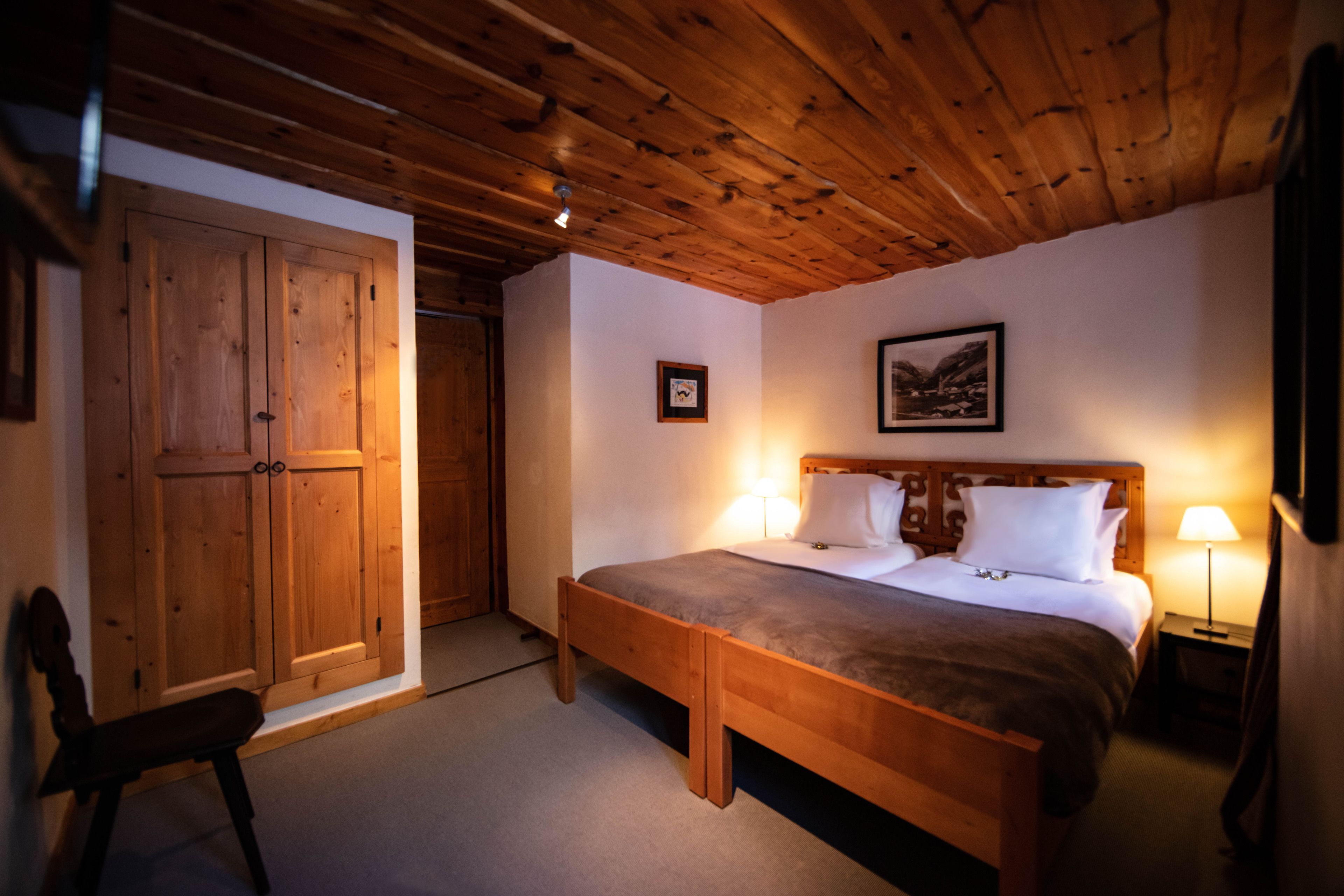 A wooden-paneled room with a bed, a chair, and a wardrobe.
