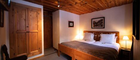A wooden-paneled room with a bed, a chair, and a wardrobe.