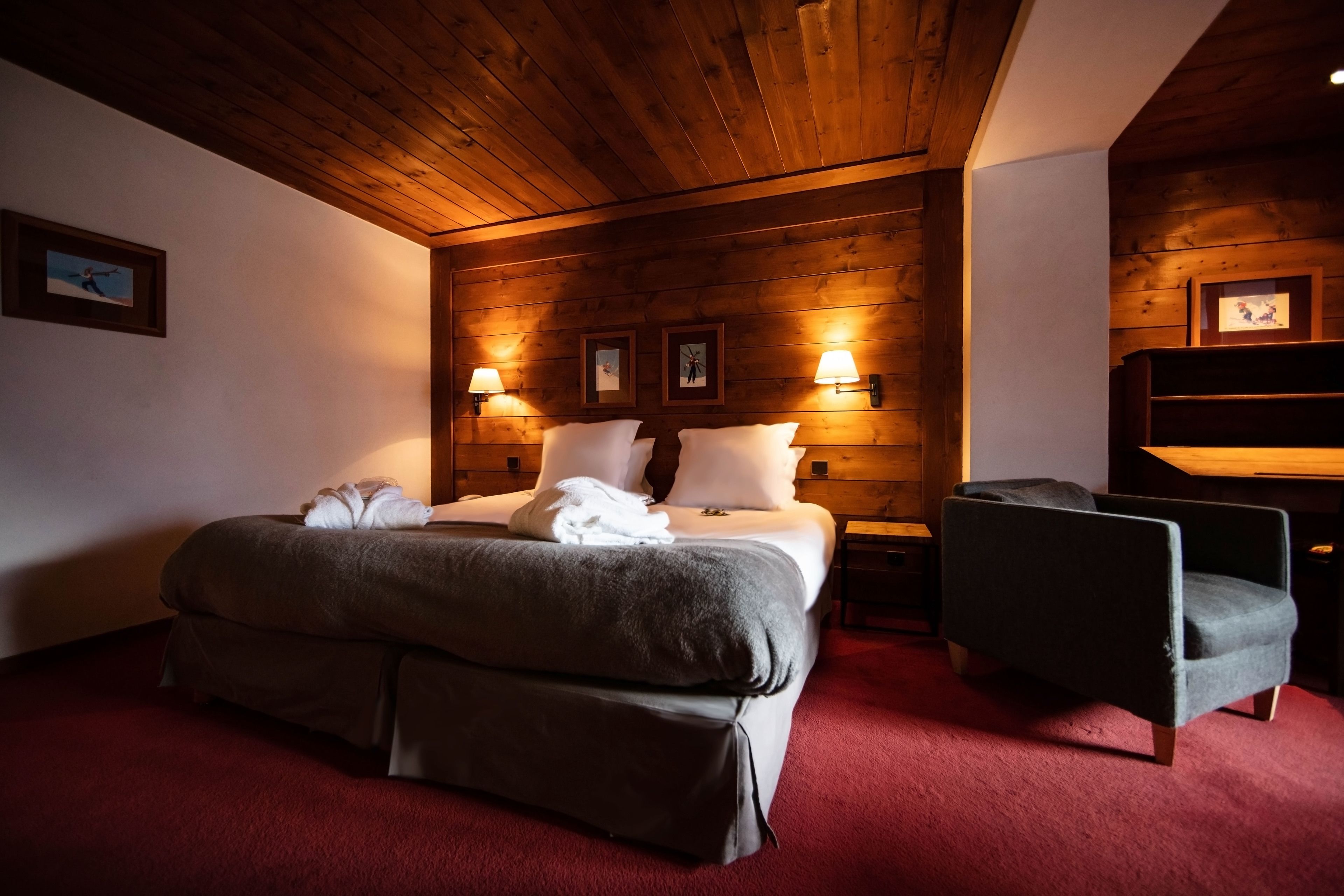 Une chambre d’hôtel avec un plafond en bois, un grand lit avec des oreillers et une couverture, deux lampes de chevet, une chaise et une petite table.