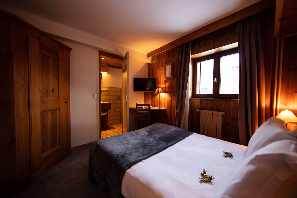 A hotel room with a bed, a desk, a television, and a window with curtains.