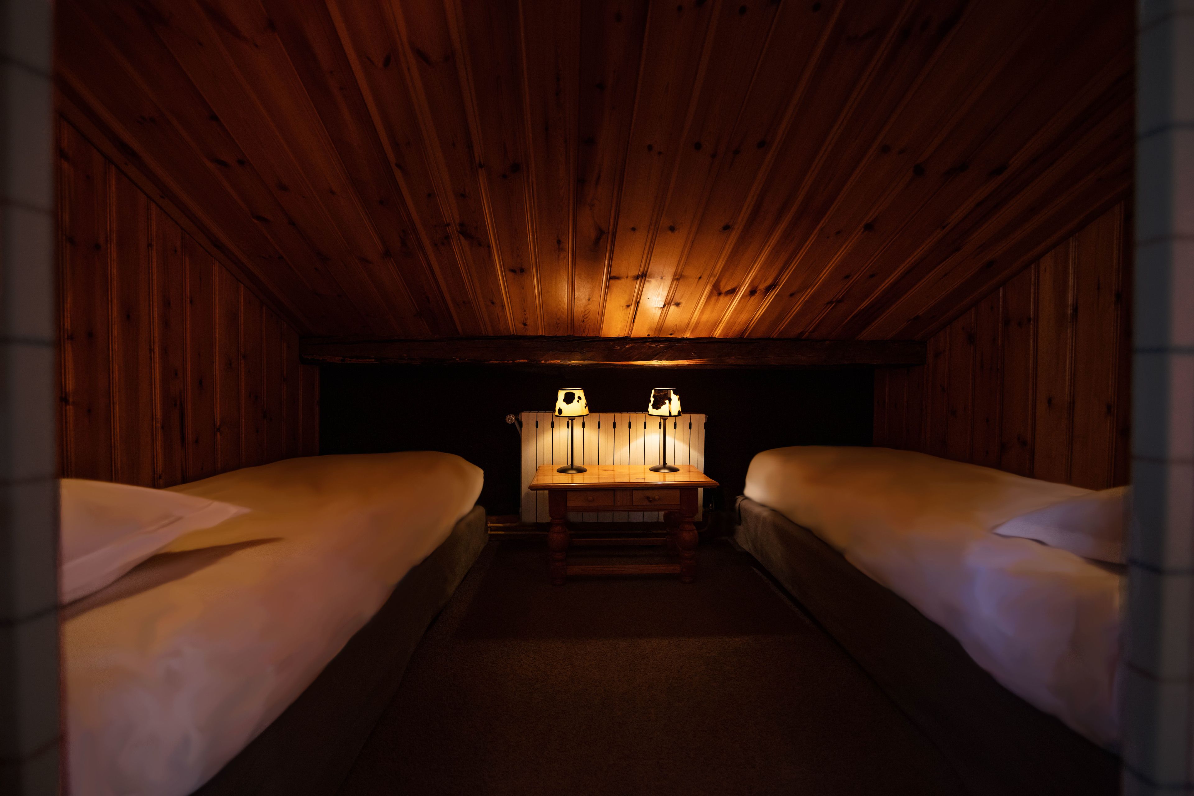 Una habitación con dos camas, techo de madera y una mesa con dos lámparas.
