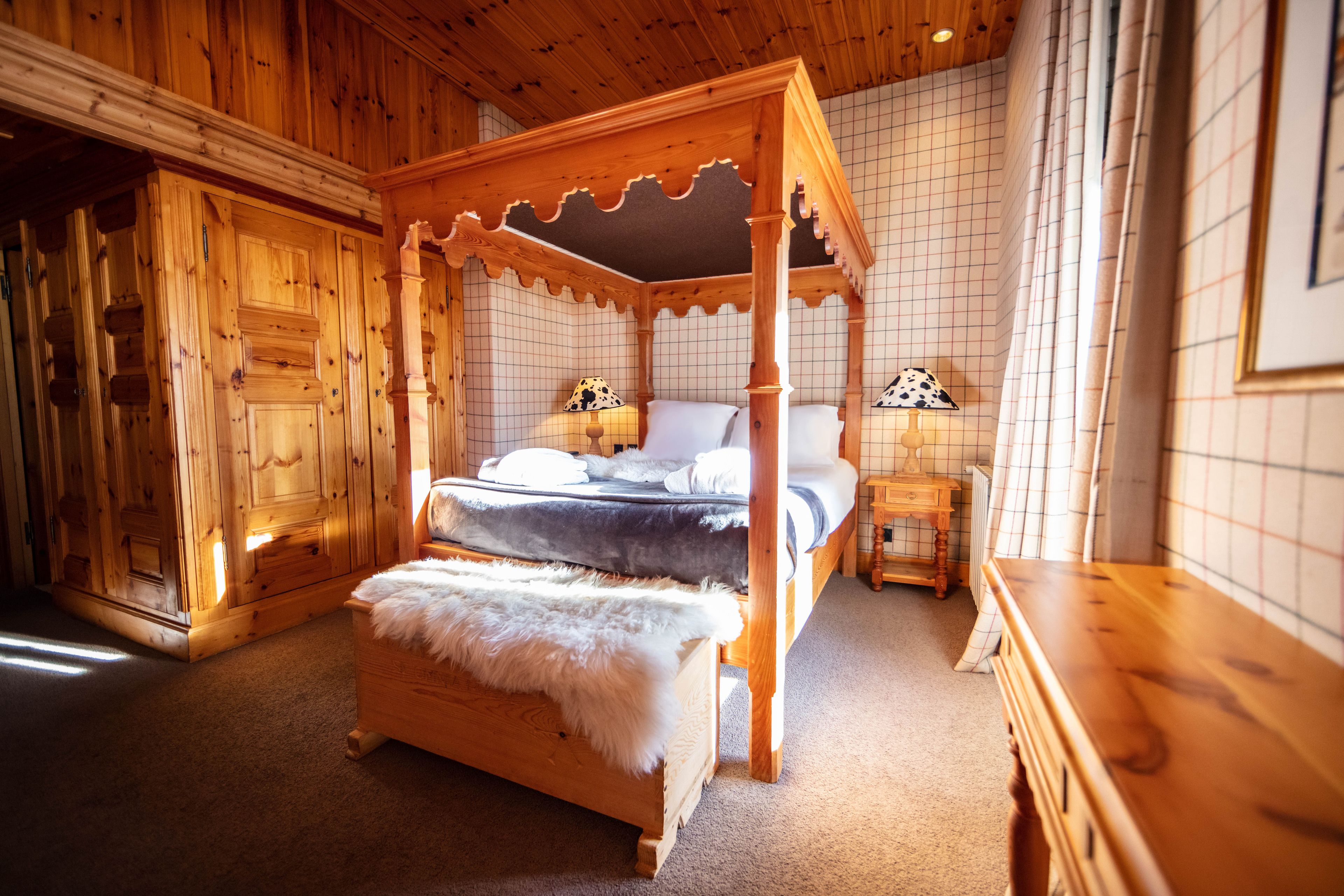 Una cama con dosel con un cubrecama de piel blanca, mesitas de noche de madera y una lámpara con pantalla de lunares.