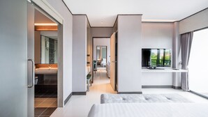 Una camera d'albergo moderna con un letto grande, una TV, un bagno con specchio e lavandino, e vista sul verde.