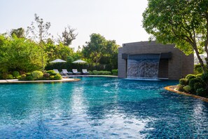 A swimming pool with a waterfall feature, surrounded by lush greenery and lounge chairs.